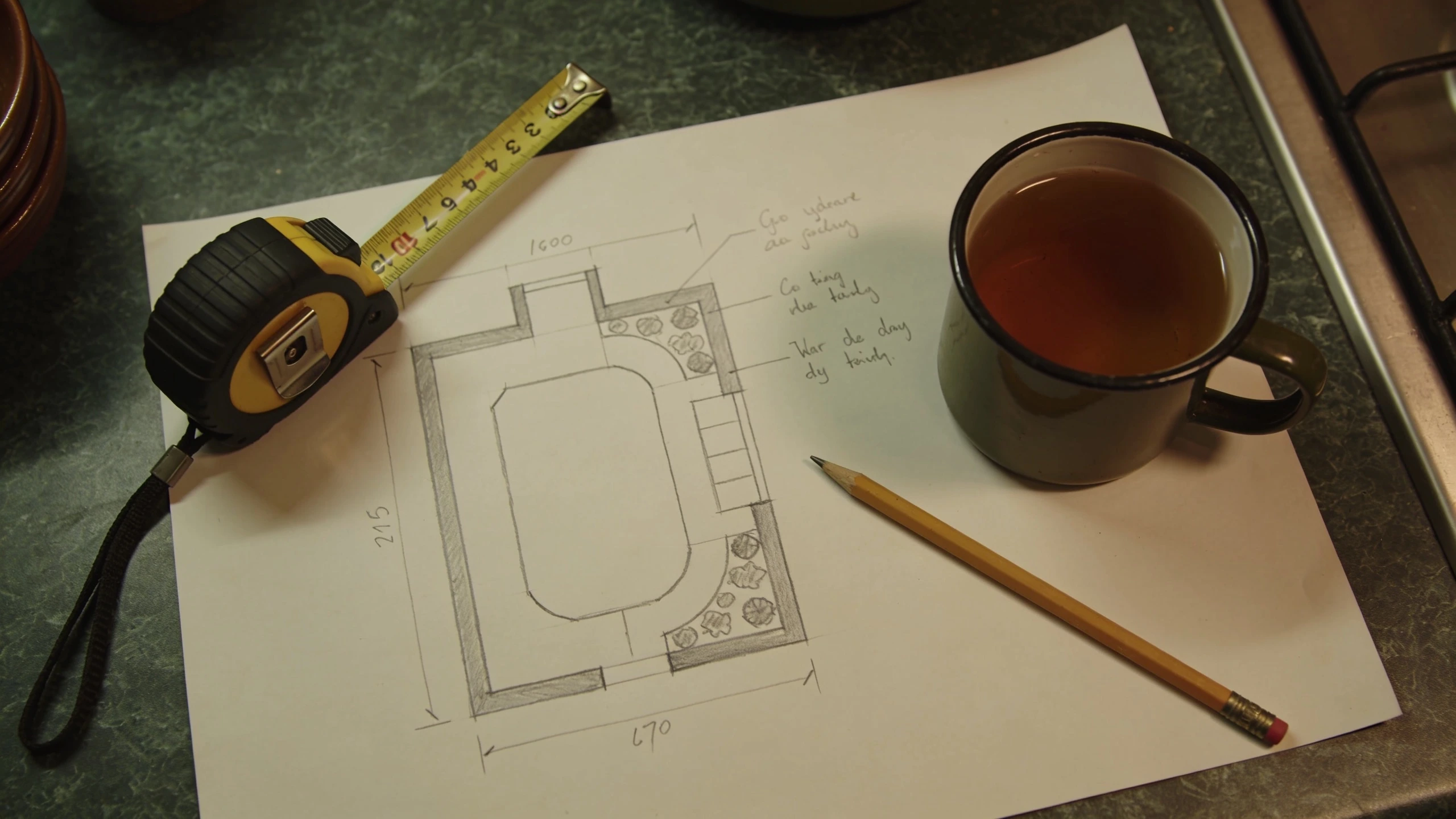 A rough plan with real measurements beats a neat drawing Hand drawn garden plan on paper with pencil measurements, a tape measure and a mug beside it
