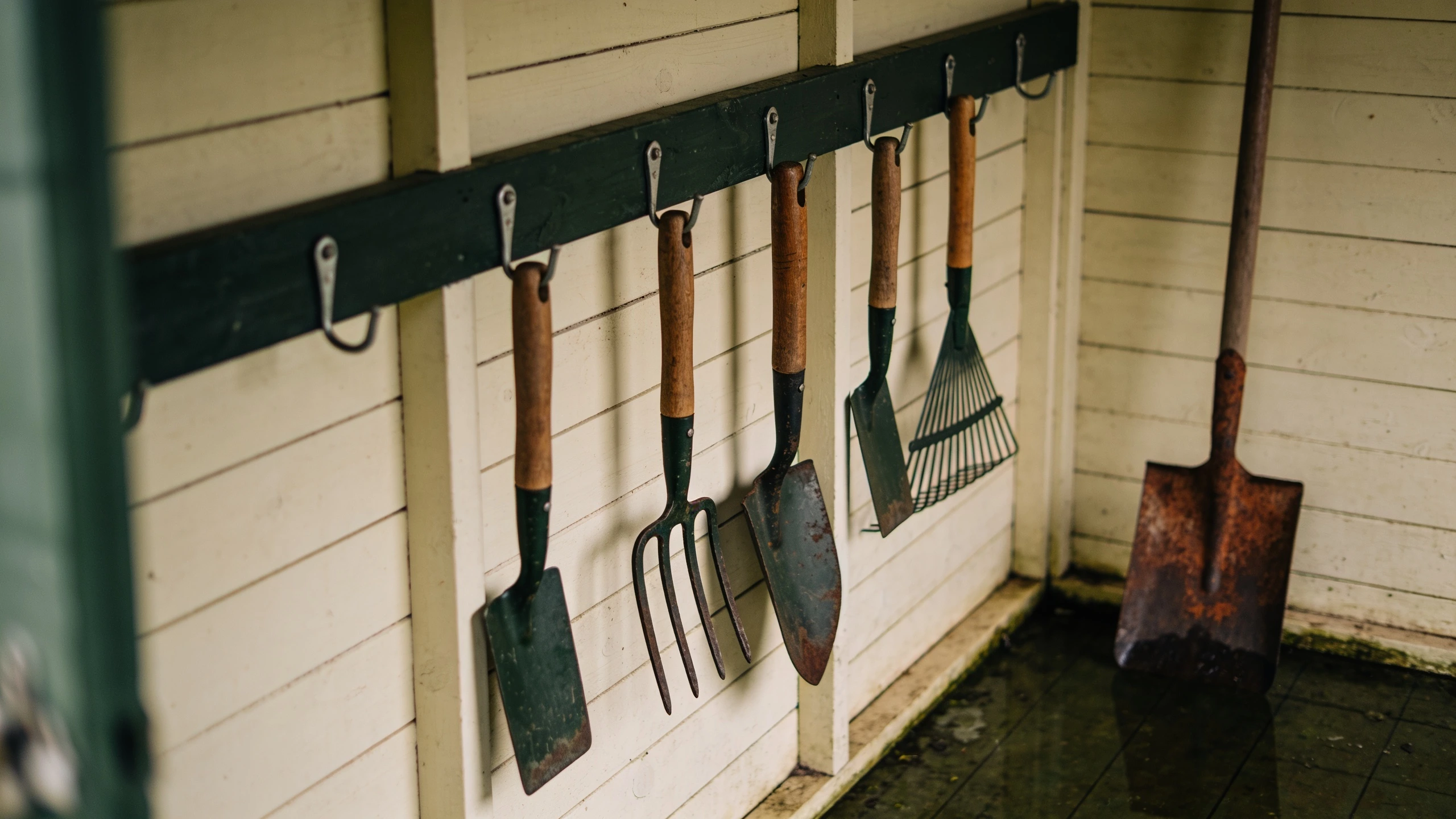 Tools hung on a wall rail rather than leaning in a corner Spade, fork, rake and hoe hanging from clips on a shed wall rail