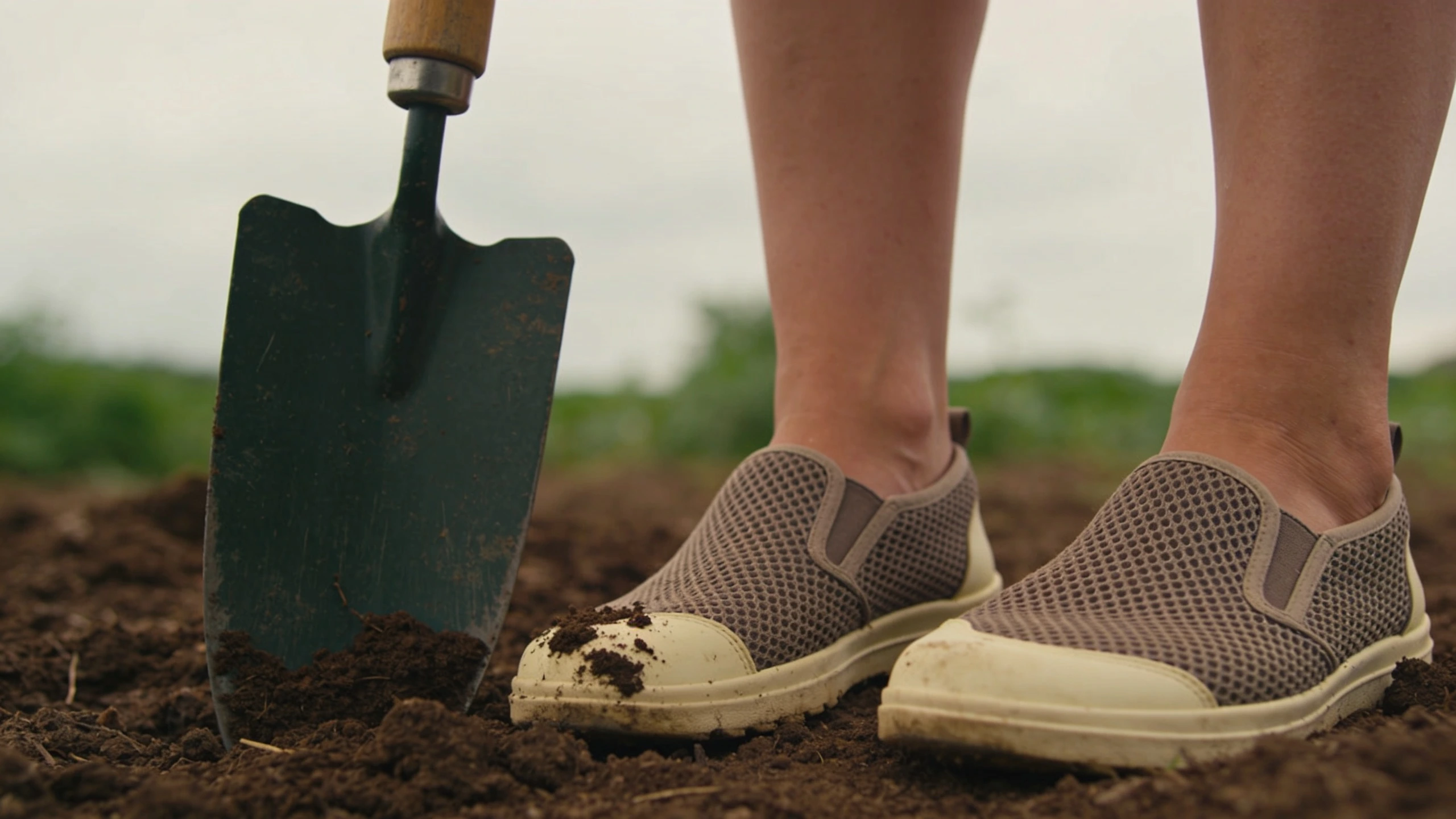 Breathable closed-toe garden shoes Mesh-panelled closed-toe garden shoes beside a spade blade stuck into soil