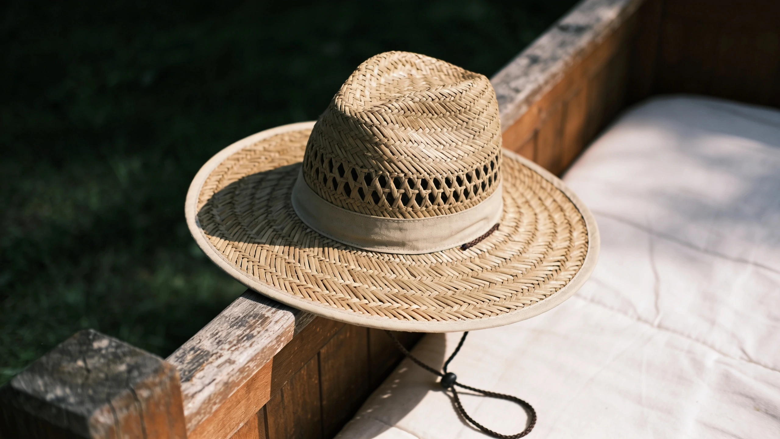 A wide-brim garden hat with a chin cord Wide-brimmed garden hat on a timber bed edge with a chin cord and vented crown