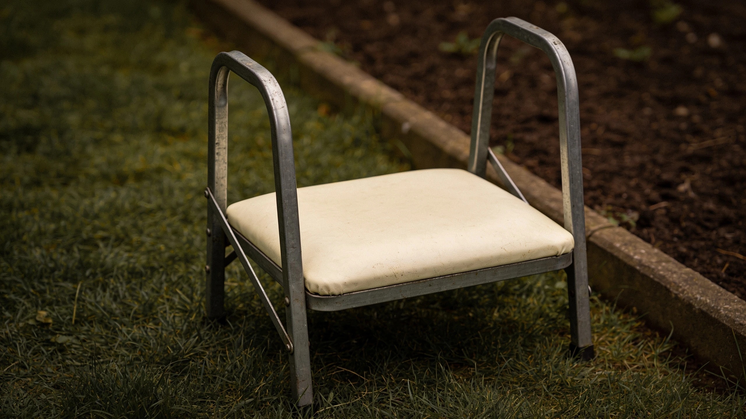 A folding kneeler-seat with push-up rails Folding steel kneeler-seat on grass with the padded panel down and side rails up