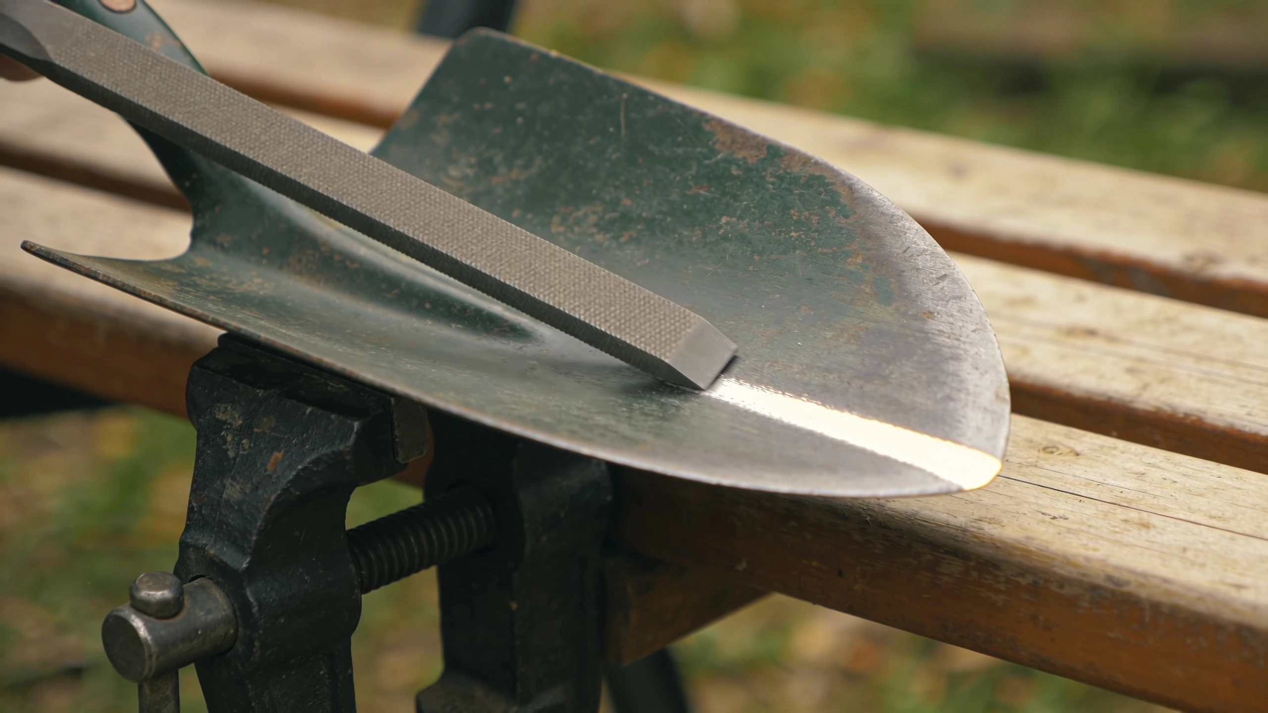 Filing the edge of a garden spade Flat mill file pushed along the inside face of a clamped spade blade at 45 degrees